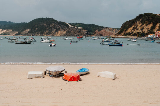 Fishing boats float in Sao Martinho do Porto Bay beside a sandy beach and waterfront buildings in Portugal. Coastal tourism connects fishing heritage with a growing seaside destination.