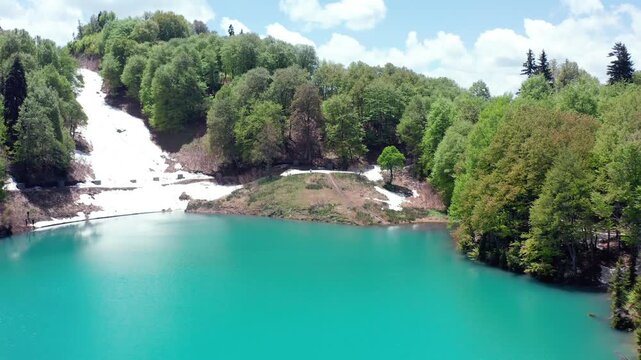 Hidden Green Lake opens in aerial view among forested slopes and melting snow near Goderdzi Pass, supporting remote tourism, hiking promotion, wilderness travel and Georgian geography content.