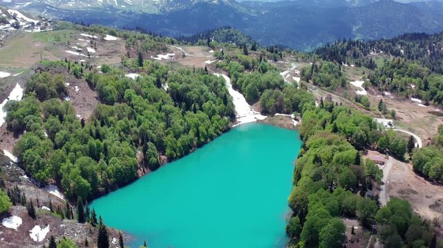 Green Lake recedes beneath descending aerial view across turquoise water, forest and snow-lined slopes in Adjara, Georgia, supporting alpine tourism, hiking promotion and remote destination media.