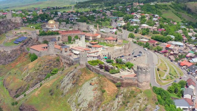 Aerial drone tracks Rabati Fortress sideways in Akhaltsikhe, Georgia, showing restored stone walls, towers, roads and surrounding homes for architectural tourism, history media and city promotion.
