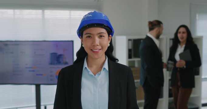 Portrait of Asian woman engineer in hard hat stands near digital screen in boardroom. Korean female manager with colleagues at project presentation in office