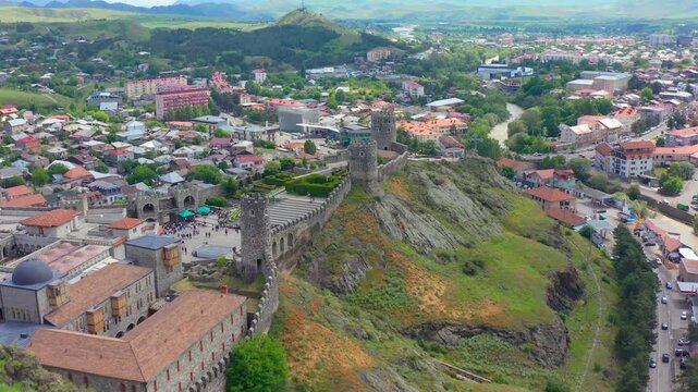 Akhaltsikhe city recedes in aerial view beside Rabati Fortress and its rocky ridge, supporting urban tourism, regional geography, heritage documentaries and destination marketing for southern Georgia.