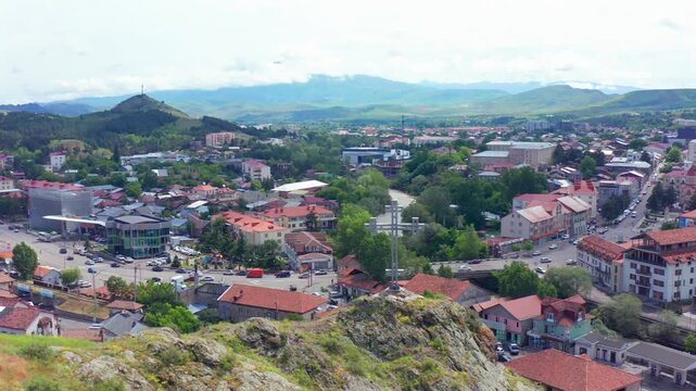 Akhaltsikhe city expands beneath descending aerial view around Rabati Fortress, red roofs and green hills, supporting city tourism, travel planning, regional geography, Georgian destination campaigns.