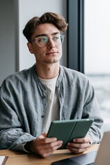 Obraz na płótnie Canvas Young man holding tablet in bright windowed cafe portrait for website banner background and professional profile design