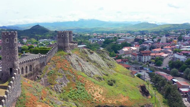 Rabati watchtower approaches in aerial view along a rocky ridge above Akhaltsikhe homes, supporting medieval architecture, Georgian heritage travel, city history, cultural tourism, landmark promotion.