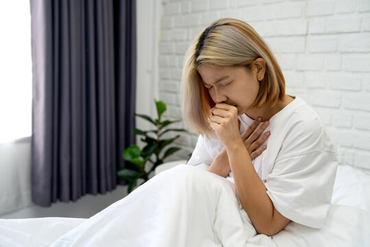 Beautiful Asian woman in pajamas feels uncomfortable sitting on the bed in her bedroom.