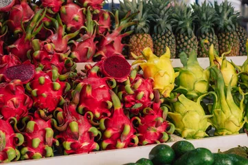 Vibrant tropical market scene featuring red and yellow dragon fruits, pineapples, and fresh exotic produce arranged for sale. © olinchuk