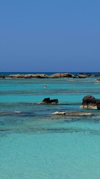 Vertical video of blue lagoon of Elafonisi beach with pink sand and black rocks. Crete. Greece