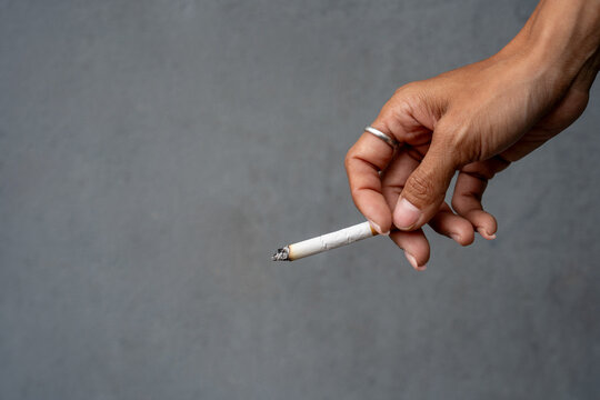 Woman's hand holding a cigarette, and the cigarette is burning.