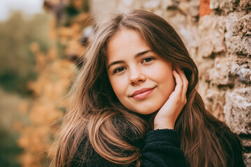 Obraz premium Young girl with long brown hair smiling against an old stone wall enjoying autumn days outdoor