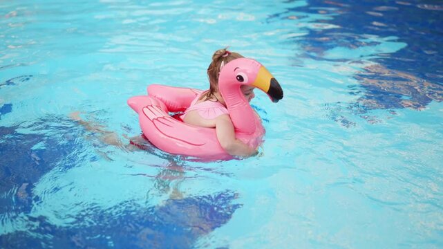 Child enjoys swimming in a pool with a flamingo float during summer time