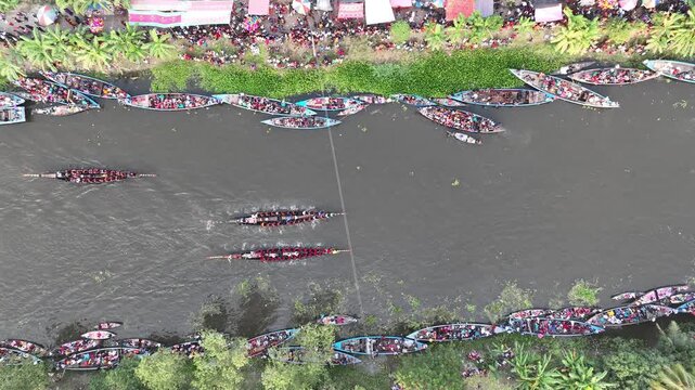 Gopalganj, Bangladesh - 30 October 2023: Aerial view of a traditional boat race on the river with many long wooden boats filled with rowers and spectators along the banks.
