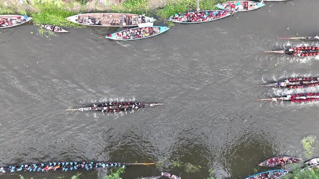 Gopalganj, Dhaka Division, Bangladesh - 30 October 2023: Aerial view of a traditional boat race with many people rowing long wooden boats along the river.