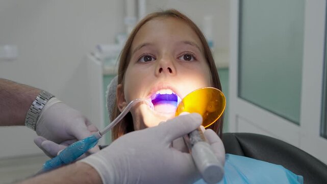 Pediatric dentist using UV curing light lamp on tooth filling for young girl.