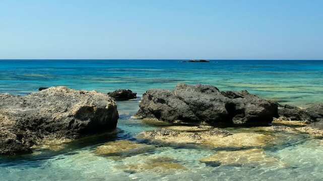 Video of blue lagoon of Elafonisi beach with pink sand and black rocks. Crete. Greece. Zoom effect.