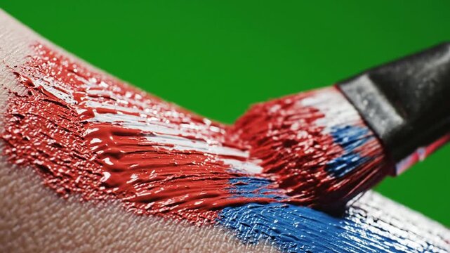 Macro close-up of paintbrush applying red and blue paint on skin, artistic body painting texture, creative makeup concept, vibrant color stroke