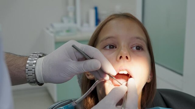 Pediatric dentist polishing tooth filling with handpiece for young girl close up