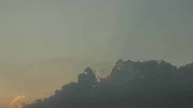 Dark cumulus clouds with glowing silver lining against a warm evening sky at sunset