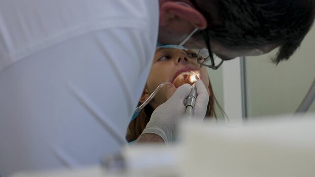 Pediatric dentist polishing tooth filling with handpiece for young girl close up