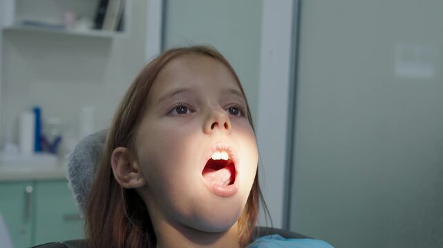Pediatric dentist polishing tooth filling with handpiece for young girl close up