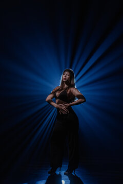 Expressive female dancer posing on dark stage illuminated by deep blue light rays. Concept of commercial artwork template for music album cover, theater flyer and creative show promotion.