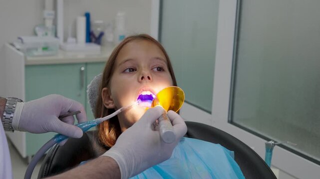 Pediatric dentist using UV curing light lamp on tooth filling for young girl.