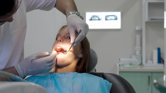 Pediatric dentist examining teeth with mirror and probe for young girl