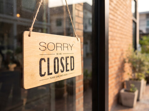 Wooden "Sorry we are closed" sign hanging on the glass door of a cafe or retail store, Closed sign board hanging outside a restaurant window with blurred brick wall background.