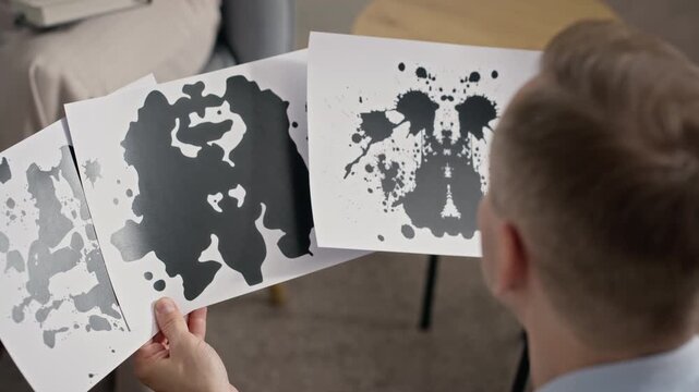 Adult Caucasian man holding and examining inkblot test cards during psychological evaluation. Video is perfect for mental health campaigns and clinical psychology concepts