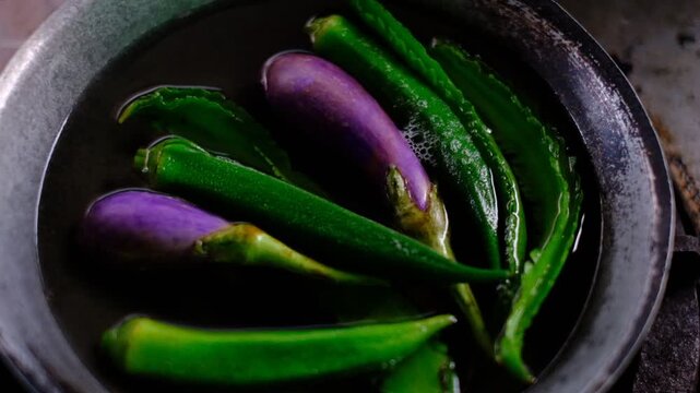 Close-up of okra and eggplant soaking in water inside weathered bowl
