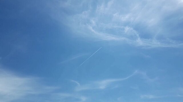 A vast, bright blue sky adorned with wispy white clouds (cirrus clouds). Amidst the serenity of this aerial landscape, an airplane is visible in the distance,