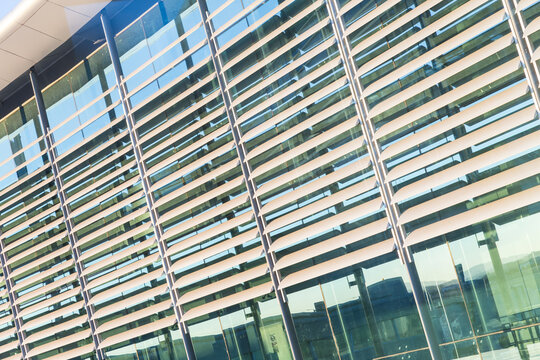 Curved exterior glass facade of a modern corporate office building featuring horizontal metal sun louvers and steel support columns reflecting sunlight.
