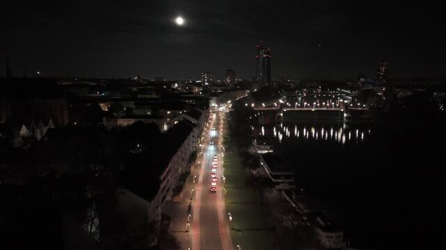 Frankfurt am Main, Hessen, Germany - 01 October 2023: Aerial view of the city skyline and Main river at night with illuminated bridges and city lights under a full moon.
