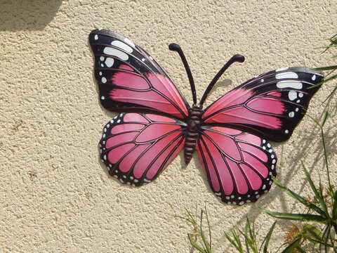 Gros plan d&rsquo;un papillon d&eacute;coratif rose et noir fix&eacute; sur un mur clair, d&eacute;coration color&eacute;e apportant une touche printani&egrave;re et originale &agrave; un espace ext&eacute;rieur.