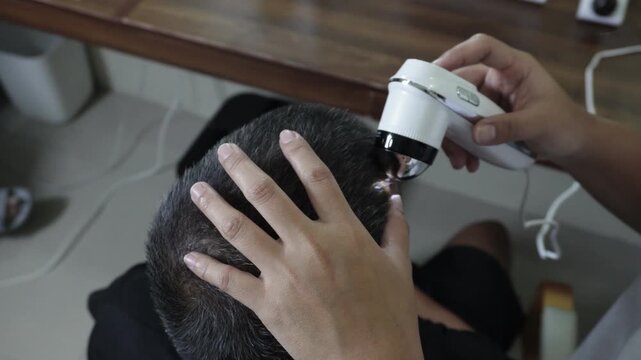 Close up of digital scalp analyzer examining a healthy middle aged man&rsquo;s scalp and hair follicles for scalp assessment and hair wellness monitoring.
