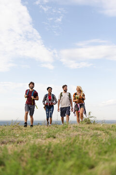 A diverse group of four friends enjoys a hike on a grassy hillside, capturing the joy of outdoor adventure in bright sunlight.