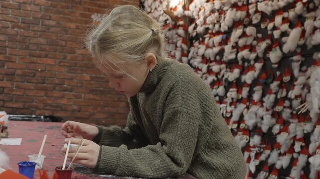 A nine year old girl makes festive Christmas crafts at a workshop table inside Santa Claus Village in Rovaniemi, Finland, surrounded by handmade ornaments on the wall