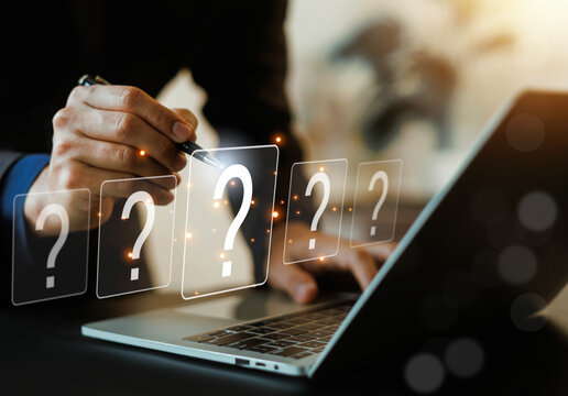 Businessman using a pen pointing at virtual question mark icons floating above a laptop. Concept of FAQ, problem solving, customer inquiry, troubleshooting, and business strategy decision.