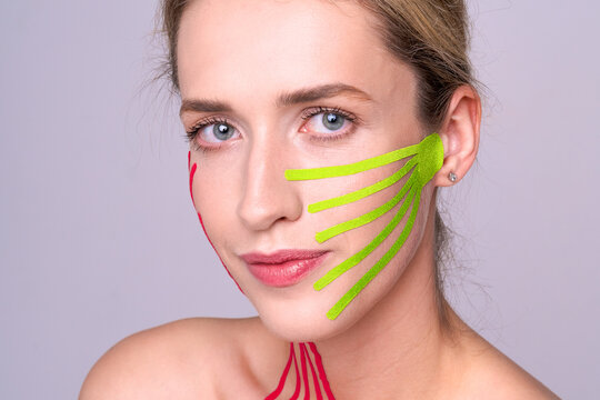Young woman with bright tapes on her face smiling on neutral background. Concept of lifting care, face taping, modern cosmetology and natural beauty