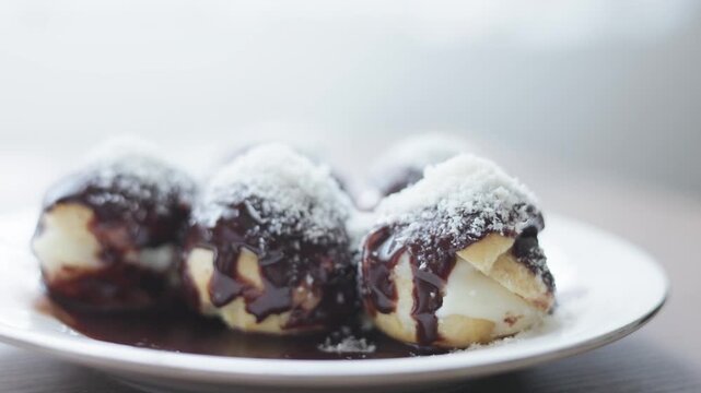 Close-up of profiteroles with chocolate sauce on white plate