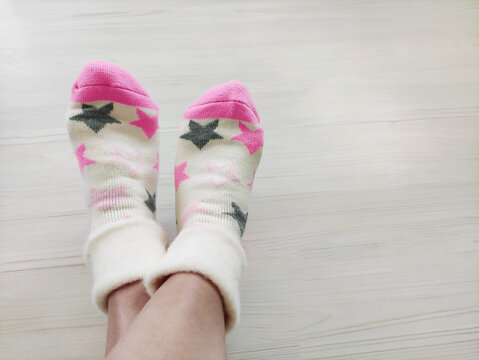 Feet wearing soft knitted patterned socks on a light wooden floor. Cozy domestic shot from a side view, concept of comfort, warmth, relaxation, leisure, and casual home fashion