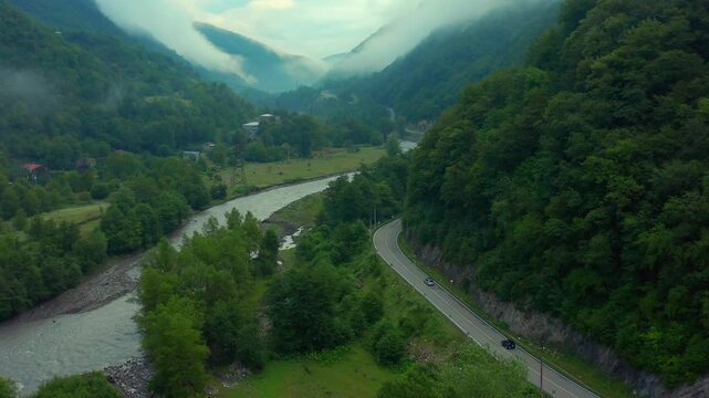 Drone flies forward above the Aragvi River valley in Georgia, following a winding mountain road through dense forest and low clouds for scenic travel, transport and destination marketing campaigns.