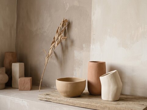 Minimalist ceramic vases and bowl. Neutral home decor with dried plant on textured wall.