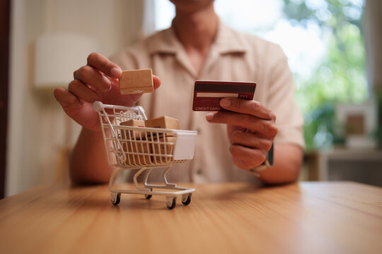 Man holds a credit card beside a shopping cart for online purchasing, representing secure digital payment, e-commerce, fast delivery, and convenient cashless shopping.