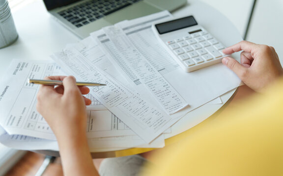 Asian Person reviewing household bills with a calculator to manage expenses, budgeting and monthly financial planning.