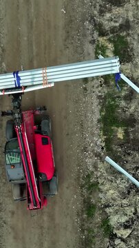 Latvia - 04 December 2024: Aerial view of a red telehandler transporting metal beams along a dirt path at a construction site.