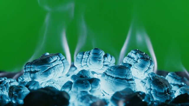 Glowing hot charcoal coals with rising smoke isolated on green screen chroma key background, embers fire