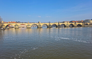 Obraz premium View of an old stone arch bridge over a river in Prague Praha European city seen from the below on the water with architectural beauty