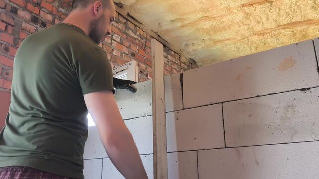 Professional builder laying aerated concrete blocks to construct interior partition walls inside a new residential building. Masonry work during house construction using lightweight gas concrete block