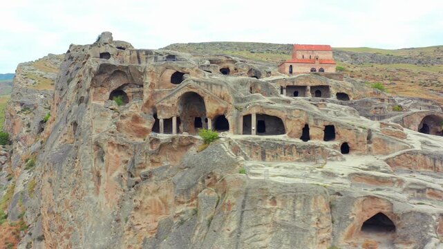 Rock-cut chambers line elevated aerial view across Uplistsikhe cliffs and ancient passageways near Gori, supporting cave architecture, archaeological research and heritage travel media campaigns.